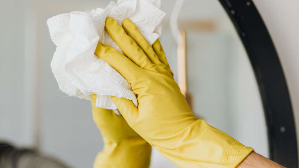 A persons hand with glove cleaning a mirror